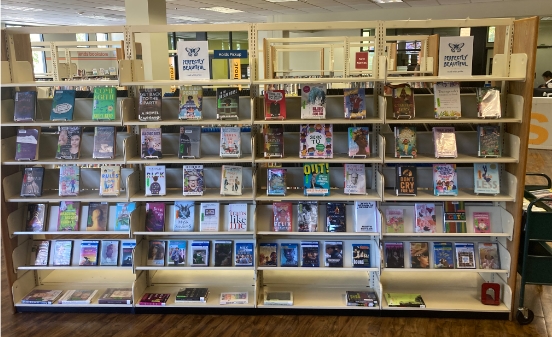 A set of four tall bookcases in the public library with faced out copies of LGBTQ+ books and films for PRIDE month